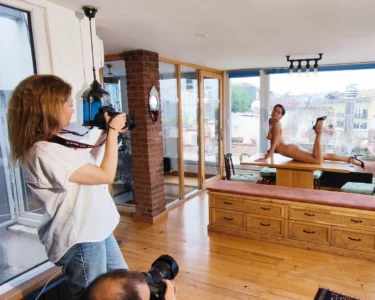 Photographer taking a nude model’s portrait in a studio with large windows