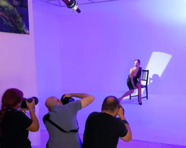 Photographers taking portraits of a seated model in a studio with purple lighting
