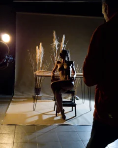 Nude model posing on a stool during a studio photo shoot