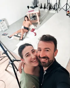 Couple taking a selfie in a photo studio, with a model posing on the floor behind them