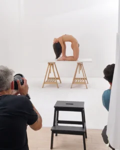 A nude model arches backward on a table while photographers take pictures in a studio
