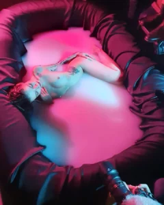 Nude woman lying in a pink-lit foam pit while being photographed from above