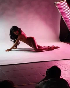 Model posing nude on a studio backdrop with pink lighting
