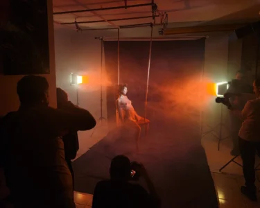 Model posing in a smoky studio while photographers shoot her under orange lighting