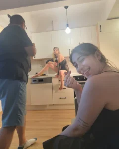 Three people in a kitchen, with one woman smiling at the camera and another sitting on the counter holding a wine glass