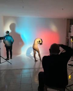 Nude model posing in a studio during a photo shoot with colored lighting