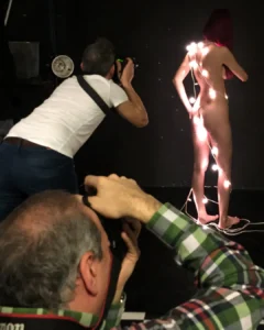Photographers taking pictures of a nude model wrapped in string lights