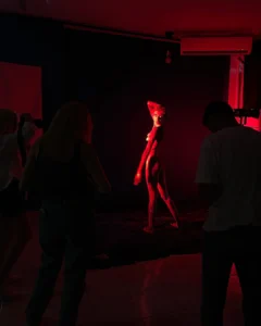 A model poses under red studio lighting while photographers watch and take pictures